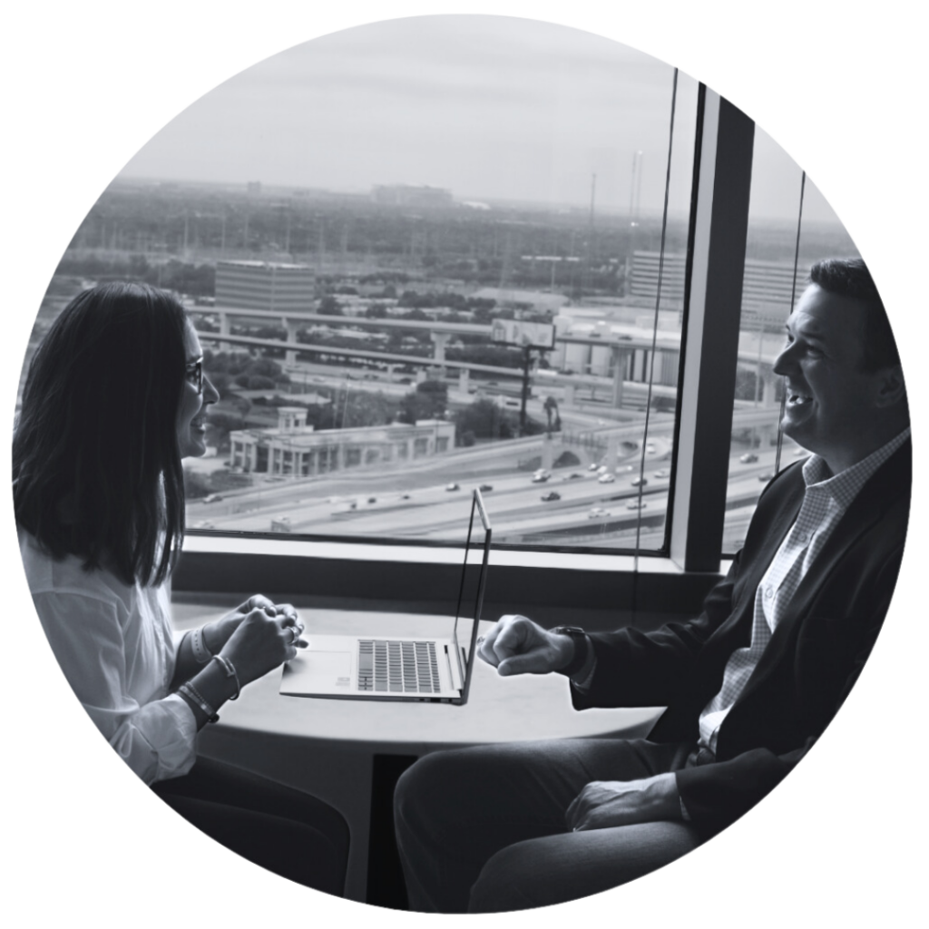 Two people sitting across a table while collaborating on a laptop in front of a window.