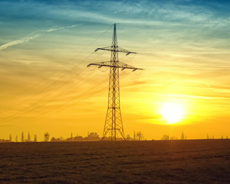 Electric tower and wires in an open field at dusk.